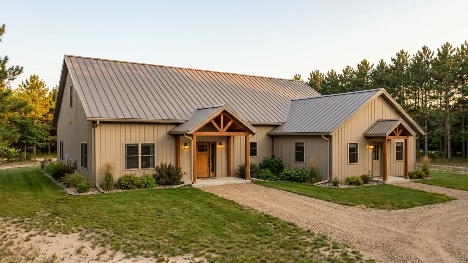 A barndominium with a smaller attached in-law suite wing that has its own covered entry, set against a stand of red pine.